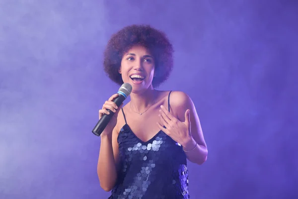 Stock image Curly young woman with microphone singing on purple background