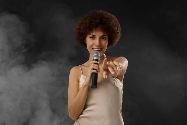 stock image Curly young woman with microphone singing in smoke on black background