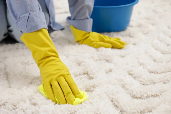 Woman in rubber gloves cleaning carpet with rag, closeup. Space for text