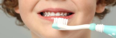 Küçük çocuk açık gri arka planda plastik diş fırçasıyla dişlerini fırçalıyor. Yakın plan. Pankart tasarımı