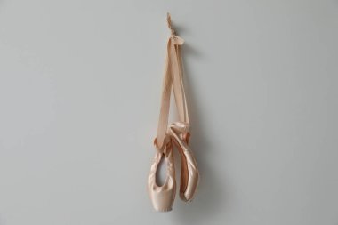 Açık gri duvarda asılı şirin kurdeleleri olan güzel bej bale ayakkabıları.