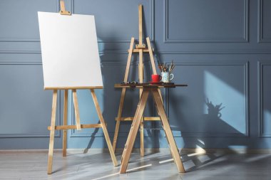 Boş tuval ve farklı sanat malzemeleri ile Easel ahşap masa kapalı gri duvar yanında