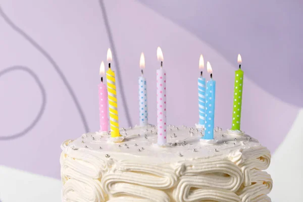 Delicious cake with cream burning candles on color background, closeup