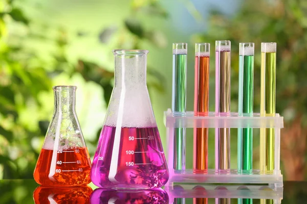 屋外のガラステーブルの上にカラフルな液体と実験室のガラス製品や試験管 化学反応 — ストック写真