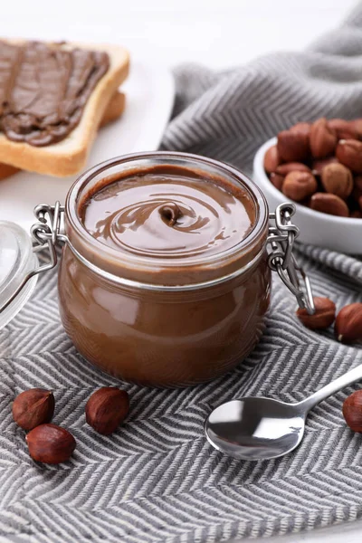 Jar with chocolate paste, tasty toast and nuts on table