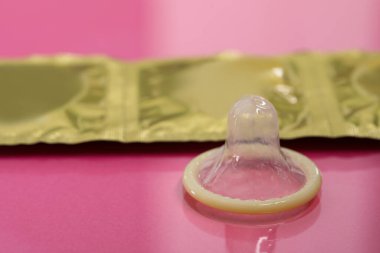 Pembe arka planda paketsiz prezervatif ve paketler, yakın plan. Güvenli seks.