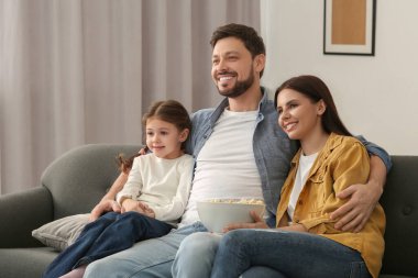 Mutlu bir aile evdeki kanepede televizyon izliyor.