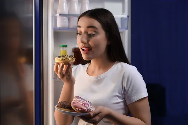 年轻女人晚上在厨房冰箱边吃甜甜圈 坏习惯 — 图库照片