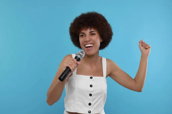 stock image Curly young woman with microphone singing on light blue background