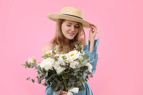 ピンクの背景に花の花束とわら帽子の美しい女性 — ストック写真