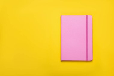 Sarı arka planda kapalı pembe defter, üst manzara. Metin için boşluk