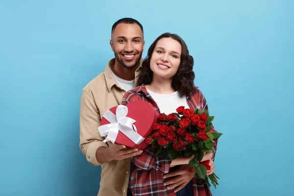 ギフトボックスと明るい青の背景に赤いバラの花束を持つ素敵なカップル バレンタインデーのお祝い — ストック写真