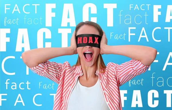 Ignoring facts. Woman wearing blindfold with word Hoax on blue background