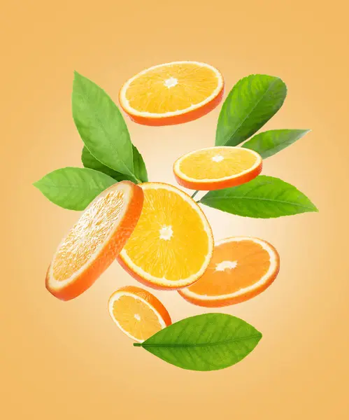 オレンジの薄切りと緑の葉が淡いオレンジの背景を飛んでいる — ストック写真