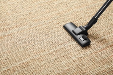 Bej halıyı modern elektrik süpürgesiyle süpürüyor. Metin için boşluk