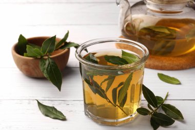 Taze demlenmiş çay, çaydanlık ve defne yaprakları beyaz ahşap masada, yakın plan.