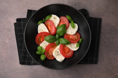 Domatesli Caprese salatası, mozzarella, fesleğen ve baharatlar kahverengi masada.