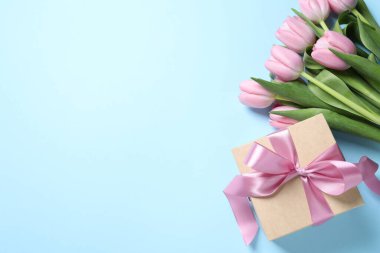 Güzel bir hediye kutusu ve açık mavi arka planda pembe lale çiçekleri. Metin için boşluk