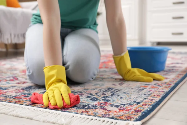 Woman in rubber gloves cleaning carpet with rag indoors, closeup