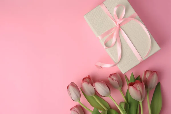 stock image Beautiful gift box with bow and tulips on pink background, flat lay. Space for text