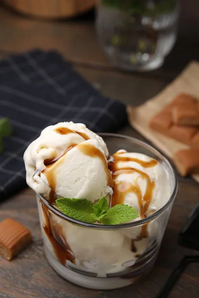 Scoops of ice cream with caramel sauce and mint leaves on wooden table, closeup