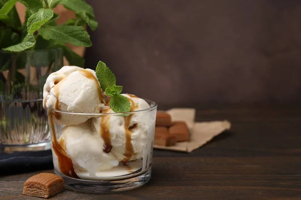 Scoops of ice cream with caramel sauce, mint leaves and candies on wooden table, closeup. Space for text