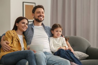 Mutlu bir aile evdeki kanepede televizyon izliyor.