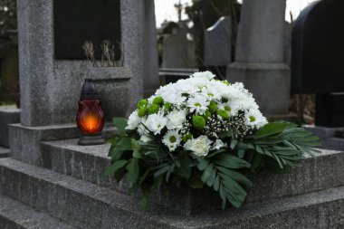 Mezarlıktaki granit mezar taşına çiçek çelengi ve mezar feneri.