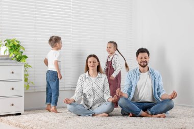 Çocuklar evde dikkatlerini dağıtırken ebeveynler meditasyon yapıyor.