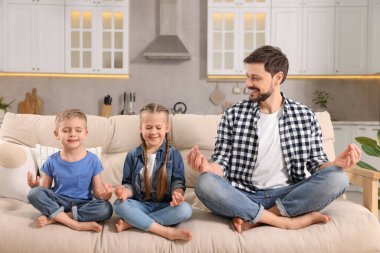 Baba ve çocuklar evdeki kanepede birlikte meditasyon yapıyorlar. Ahenk ve zen
