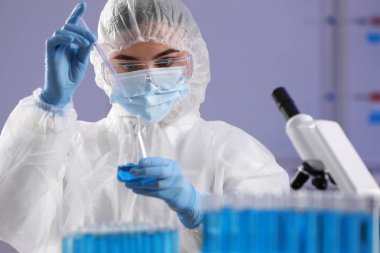 Bilim adamı laboratuvarda açık mavi sıvı örneği alıyor.
