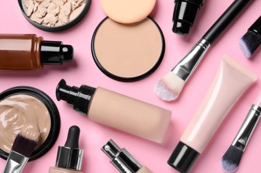 Farklı sıvı temeller, güzellik aksesuarları ve pembe arka planda yüz pudraları, düz yatış