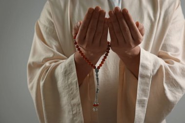 Misbaha 'lı Müslüman adam açık gri arka planda dua ediyor, yakın plan