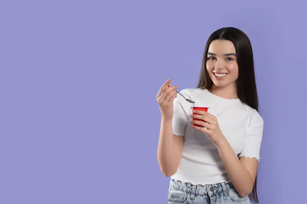 紫の背景においしいヨーグルトとスプーンを持つ幸せな十代の女の子 テキストのスペース — ストック写真