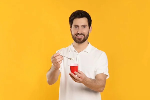 一个英俊的男人 有美味的酸奶和黄色背景的勺子 — 图库照片