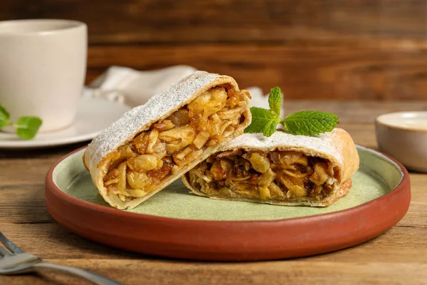 Delicious strudel with apples, nuts and raisins on wooden table, closeup