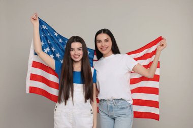4 Temmuz - ABD 'nin Bağımsızlık Günü. Açık gri arka planda Amerikan bayrağı taşıyan mutlu kadın ve kızı