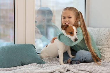 Pencerenin pervazında köpeğini kucaklayan tatlı bir kız. Sevimli hayvan.