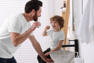 Baba ve oğlu banyoda dişlerini fırçalıyorlar.