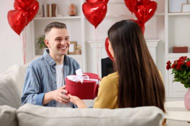 Man receiving gift box from his girlfriend at home. Valentine's day celebration