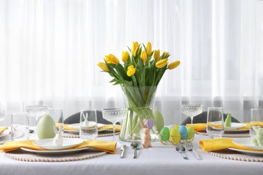 Festive table setting with glasses, painted eggs and vase of tulips. Easter celebration