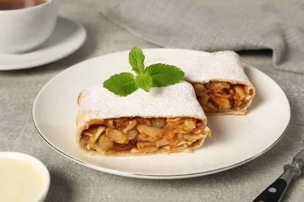 Delicious strudel with apples, nuts and raisins on light grey table, closeup