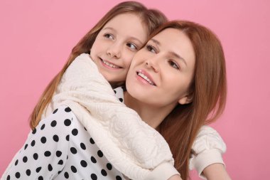 Pembe arka planda mutlu anne ve kızının portresi.