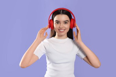 Teenage girl listening music with headphones on violet background