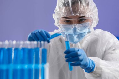 Laboratuvarda açık mavi sıvılarla test tüpleri tutan bilim adamı.