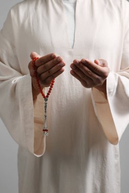 Misbaha 'lı Müslüman bir kadın açık gri arka planda dua ediyor, yakın plan