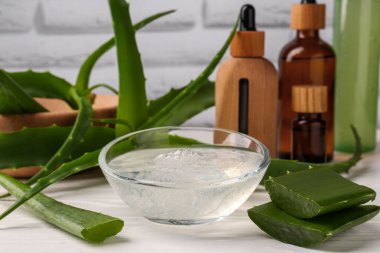Bir kase kozmetik jel ve beyaz ahşap masa üzerindeki aloe vera yapraklarını kes.
