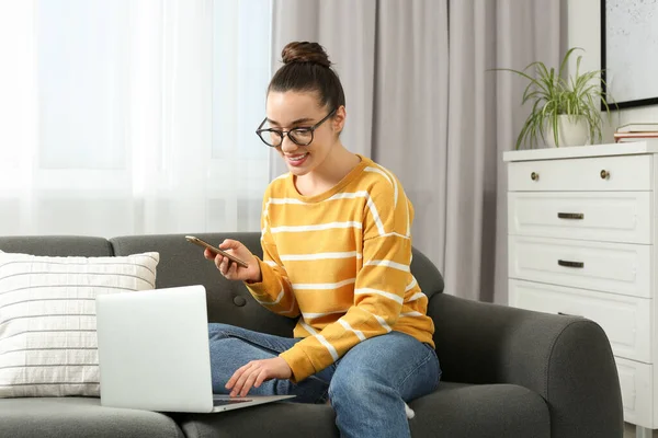 家庭工作场所有智能手机和笔记本电脑在房间沙发上的快乐女人 — 图库照片