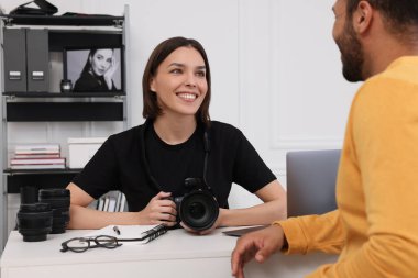 Modern fotoğraf stüdyosundaki bir adamla konuşurken elinde kamera olan genç profesyonel fotoğrafçı.