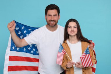 4 Temmuz - ABD 'nin Bağımsızlık Günü. Mutlu adam ve kızı açık mavi arka planda Amerikan bayrakları taşıyorlar.